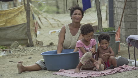 Mujer-Namibia-Cuida-A-Niños-Mientras-Hace-Tareas-Domésticas-En-Un-Barrio-Marginal-Del-Bosque:-Plano-Medio-Largo
