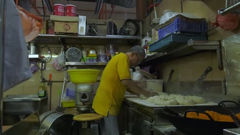 Panadero-Singapurense-Amasando-Masa-En-La-Parte-Trasera-Del-Mostrador-Del-Mercado-De-Alimentos---Plano-Amplio