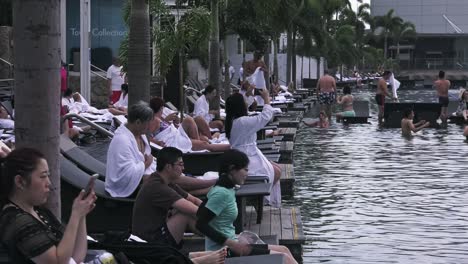 Turistas-Descansando-En-Tumbonas-Junto-Al-Borde-De-La-Piscina-Infinita-En-El-Skypark-Del-Hotel-Marina-Bay-Sands,-Singapur---Amplia-Vista-Lateral-Estática