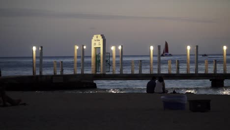 Kahanamoku-Strandpier-In-Der-Abenddämmerung-Mit-Sanften-Lichtern,-Die-Den-Weg-Leiten-–-Mittellange-Schwenkaufnahme-Von-Links-Nach-Rechts