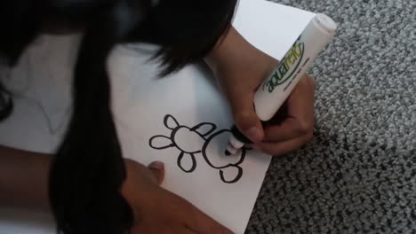 Hand-held-shot-of-a-young-girl-drawing-a-cartoon-on-paper-with-a-marker