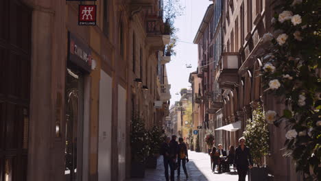 People-On-Narrow-Shopping-Alley-Adorned-With-Beautiful-Flowering-Plants-In-Daytime-In-Milan,-Italy