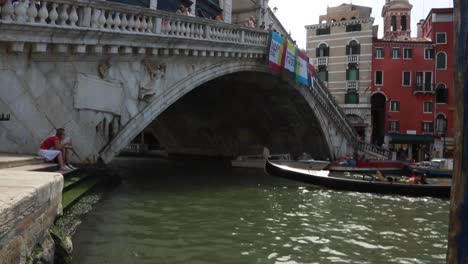 Góndola-Veneciana-Con-Turistas-Paseando-Bajo-El-Puente-De-Rialto-En-Un-Día-Soleado-En-Venecia,-Italia