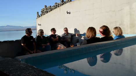 Group-of-people-sitting-around-in-ground-fire-place-next-to-pond-in-golden-sunset-light