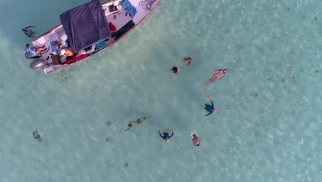 AERIAL-TOP-VIEW-ZOOM-OUT-GROUP-PEOPLE-FRIENDS-float-in-circle-flat-water-safeway-with-motorboat-in-the-middle-of-the-ocean-near