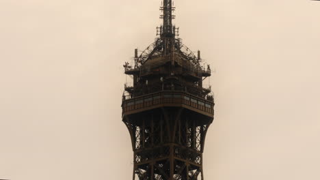 Top-Summit-of-Eiffel-Tower-in-City-of-Paris-on-Cloudy-Day,-Tilt-Up-View