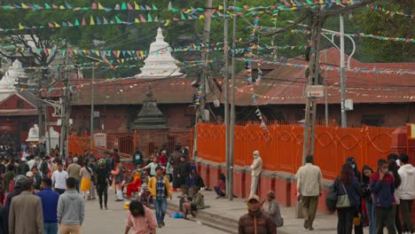 A-crowd-of-people-walking-near-temples-and-shrines-with-prayer-flags-hanging,-in-Kathmandu,-Nepal