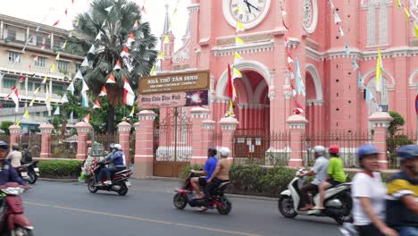 Vista-De-La-Calle-Del-Tráfico-De-Motos-Conduciendo-Por-La-Iglesia-Rosa-Del-Sagrado-Corazón-En-La-Ciudad-De-Ho-Chi-Minh,-Vietnam