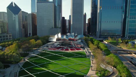 top-down-chicago-aerial-in-the-summer-above-parks-flying-backwards,-Jay-Pritzker-Pavilion,-crosswalks,-millenium-park