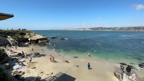 Wide-shot-of-sunny-beach-with-people-at-La-Jolla-Cove-in-San-Diego,-California