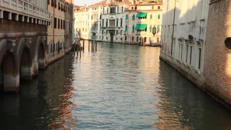 Handheld-tilt-camera-view-revealing-an-empty-and-calm-water-canal-with-classic-Venetian-architecture-buildings-in-the-background-in-Venice,-Italy