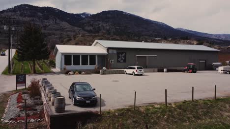 small-tin-roof-of-intersection-winery-in-okanagan-valley-amongst-vineyards-mountains-in-osoyoos-bc-canada-appraoching-aerial-4k-stabilized