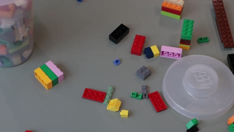 Langsame-Schwenkaufnahme-Von-Lego-Bausteinen,-Die-über-Einen-Tisch-Verstreut-Sind