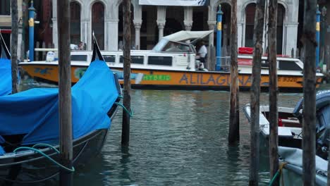 Close-shot-of-Venetian-boats-and-gondolas-docked-in-a-Grand-Canal's-pier-and-tourist-boat-passing-in-the-background-in-Venice,-Italy