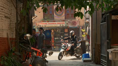 A-motorbike-entering-through-a-narrow-street-with-small-shops-and-markets,-in-Kathmandu,-Nepal