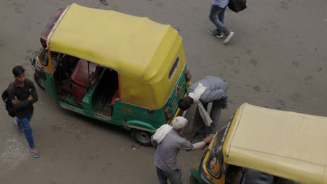 Man-cleaning-his-Tuk-Tuk-on-busy-road,-Delhi-India