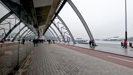 Busy-bicycle-lane-outside-of-the-Amsterdam-Central-Station-Beside-IJ-River,-as-people-go-about-their-day-commuting-on-their-bicycles-in-the-busy-urban-city,-Amsterdam,-Netherlands