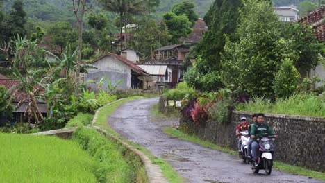 Students-on-motorbikes-pass-through-a-rural-road-in-the-hills-of-Garut,-West-Java