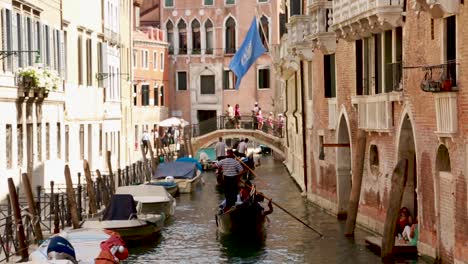 Busy-Venetian-canal-with-tourists-riding-gondolas-and-walking-in-Venice,-Italy