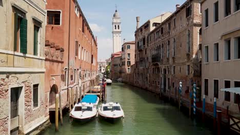 Venetian-boats-parked-in-a-calmed-and-empty-small-canal-in-Venice,-Italy