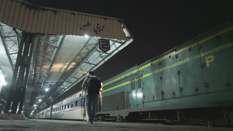 Male-Wearing-Rucksack-Walking-Along-Empty-Karachi-City-Railway-Station-Platform-At-Night