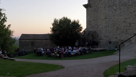 Reveal-pan-shot-of-a-crowd-watching-a-pianist-perform-in-a-castle-in-France-during-sunset