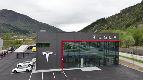 Modern-Gestaltetes-Gebäude-Mit-Glasfassade-Im-Tesla-Autohaus-In-Forde,-Norwegen-–-Luftaufnahmen-Aus-Geringer-Höhe-Zeigen-Langsam-Das-Gebäude-Mit-Reflexionen-In-Den-Fenstern