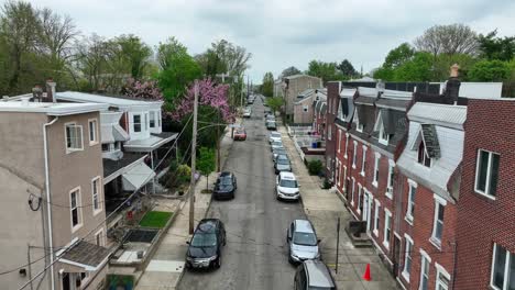 Aerial-dolly-forward-over-city-street-lined-with-houses-and-blossoming-trees-in-spring