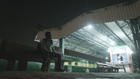 Foto-De-ángulo-Bajo-De-Un-Hombre-Sentado-En-Un-Banco-En-La-Plataforma-De-La-Estación-De-Tren-De-La-Ciudad-De-Karachi-En-Karachi,-Pakistán-Por-La-Noche