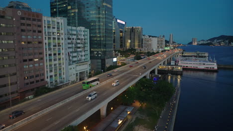 Aufsteigender-Drohnenflug-Entlang-Der-Kwun-Tong-Umgehungsstraße-Mit-Verkehr-In-Der-Abenddämmerung-In-Der-Stadt-Hongkong