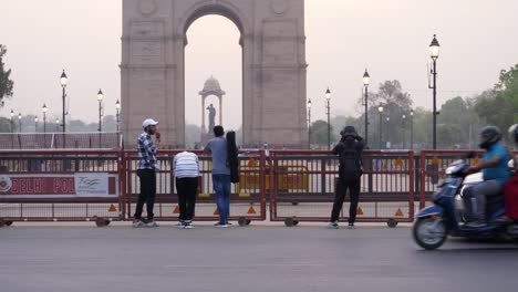 Delhi-Police-barricades-stand-at-India-Gate,-traffic-at-the-street-of-Kartavya-Path,-journalists-clicking-photographs-of-air-pollution-and-grey-sky-at-India-Gate,-Delhi