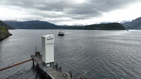 Fjord-1-Ferry-charger-on-quay-with-electric-ferry-Eidsfjord-approaching-Lote-ferry-pier-in-Nordfjord-Norway---Slow-moving-aerial-showing-arrival-of-ferryboat