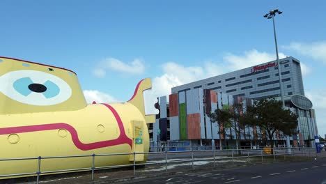 Yellow-submarine-and-Hilton-hotel-outside-John-Lennon-international-airport-glass-front-entrance,-England,-Pan-right-shot