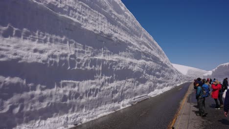 Turistas-Caminando-Por-La-Carretera-Alpina-Con-Muros-De-Nieve-En-Las-Montañas-Tateyama
