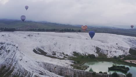 Hot-air-balloons-float-over-travertine-hot-springs-of-cloudy-Pamukkale-morning