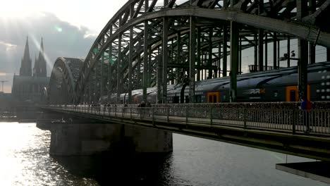 Der-Rhein-Express-Regionalzug-Fährt-An-Der-Hohenzollernbrücke-Vorbei,-Mit-Blendenflecken-In-Der-Ecke-Und-Den-Türmen-Des-Kölner-Doms-Im-Hintergrund