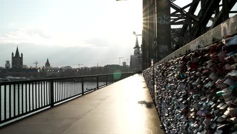 Shot-of-locals-going-about-their-day-walking-across-the-Hohenzollern-Bridge-over-river-Rhine-in-Cologne,-Germany-on-a-sunny-day