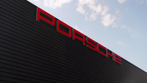 Contra-El-Cielo-Como-Telón-De-Fondo-Se-Alza-Un-Alto-Edificio-Negro-Con-El-Logotipo-De-La-Empresa-Porsche-En-Un-Lugar-Destacado.