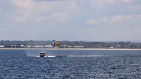 Perth-RAC-Rescue-Helicopter-Chasing-Marine-Rescue-Boat-And-Lowering-Winch-Cable,-Seen-From-Busselton-Jetty