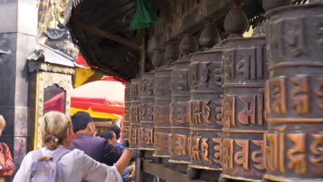 Close-Up-Of-Female-Tourists-Hands-Scrolling-Across-Row-Of-Prayer-Wheels-At-Temple-In-Kathmandu,-Nepal