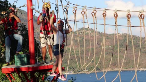 Woman-walking-fearfully-on-hanging-ropes-at-a-zip-line-recreational-park