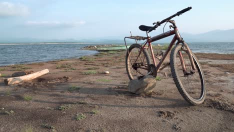 Rusty-bicycle-parked-on-a-stone-near-a-fishing-boat-near-the-ocean-shore,-Dolly-right-shot
