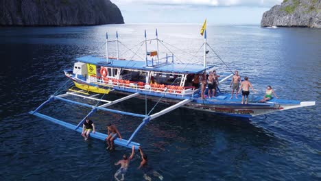 Group-of-young-tourists-People-swimming,-jumping-off-island-hopping-tour-boat-into-tropical-seawater,-El-Nido---Philippines