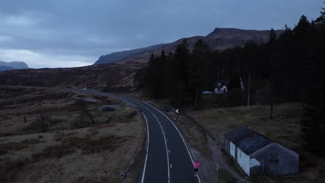 Ein-Einsamer-Jogger-Läuft-Die-Hauptstraße-Von-Glencoe-In-Schottland-Entlang,-Luftaufnahmen