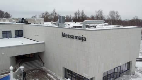 Metsamaja-main-entrance-with-flags-flown-over-drone,-great-aerial-shot,-we-can-also-see-Europe,-Estonia-and-EMÜ-flags