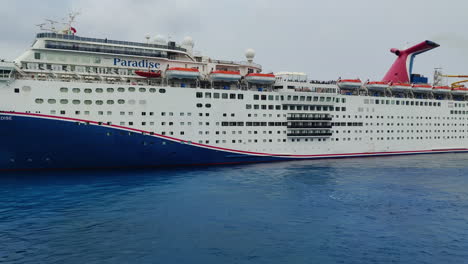 Luxury-cruise-ship-Carnival,-Paradise-moving-backwards-near-a-port-in-Cozumel,-Mexico-|-Cruise-ship-Carnival-moving-in-ocean-close-up-shot-cinematic-video-in-4K