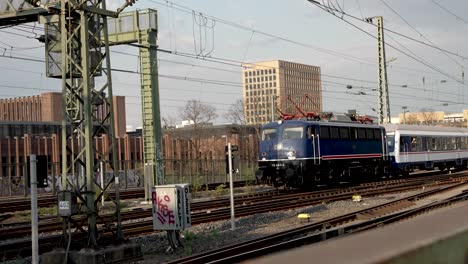 Vintage-Retro-Blue-Train-Pulling-Passenger-Carriages-On-Railway-Lines-Towards-Cologne-Central-Station
