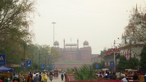 People-walking-on-the-street-of-newly-developed-Chandni-Chowk-in-old-Delhi,-view-of-Red-Fort-in-the-background-in-hazardous-air-pollution,-grey-smog,-mist-sky,-India