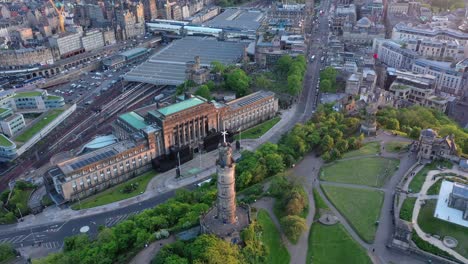 Edinburgh-Waverley-Train-Station-wide-aerial-shot,-calton-Hill-and-Nelson-monument-by-drone