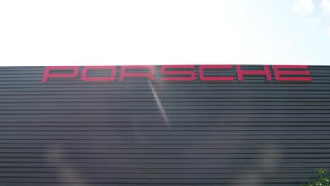 Porsche-Händlergebäude-Vor-Der-Einrichtung,-Großes-Porsche-Logo,-Carrera,-Panamera,-Taycan,-Turbo,-Sportwagen,-Motor,-Autos,-Nach-Oben-Geneigte-Aufnahme,-Außenansicht-Des-Ausstellungsraums